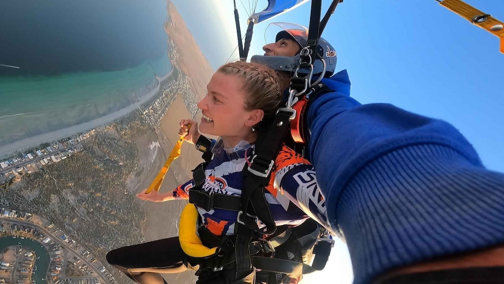 A person skydiving with a parachute, overlooking a coastal landscape with buildings and a beach. 1
