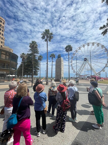 A group of people standing in a plaza with a Ferris wheel and palm trees in the background. 3
