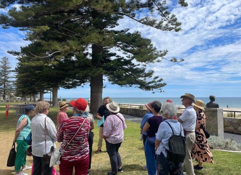 A group of people gathered around a large tree by a coastal walkway. 5
