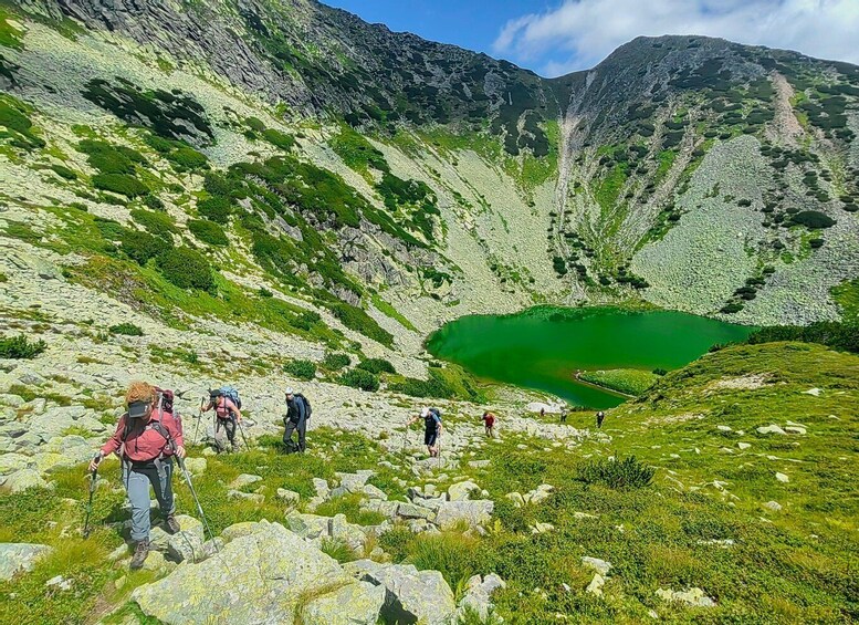 Hikers on a rocky mountain trail with a green lake in the valley. 1