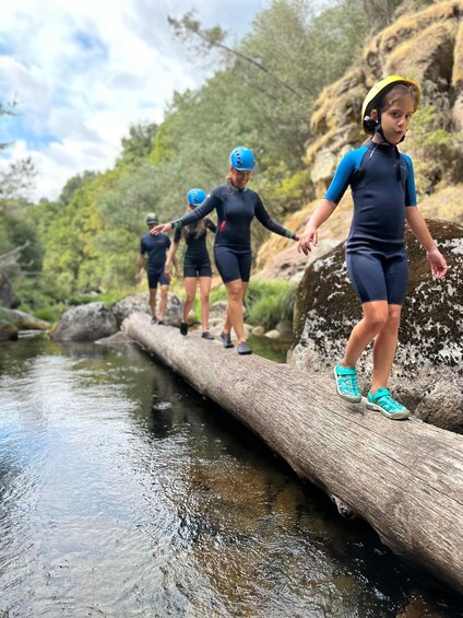 People walking on a log over a stream in a forested area. 3