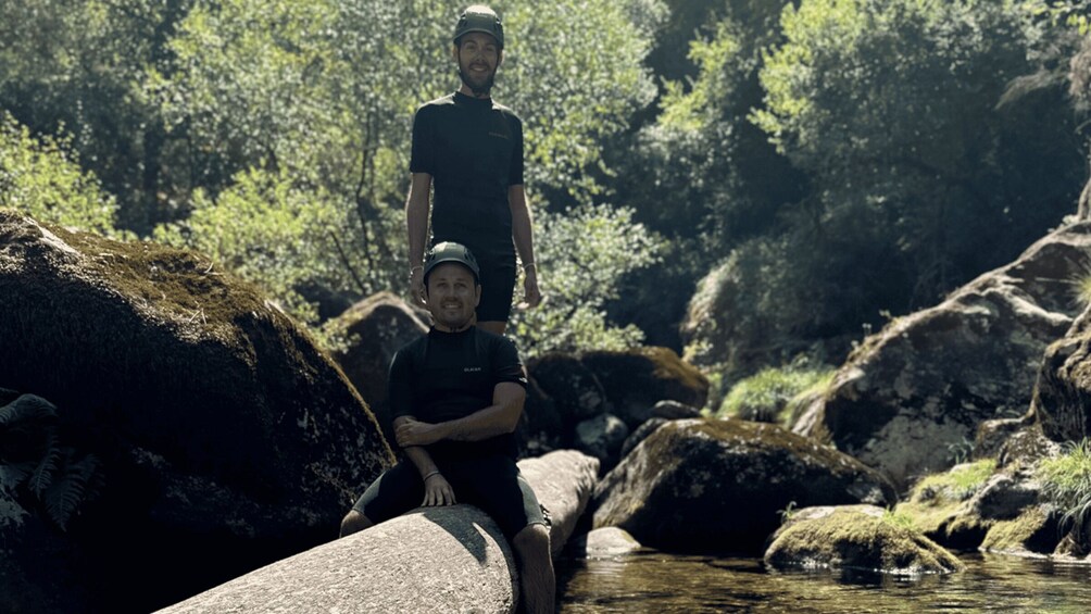 Two people sitting on rocks by a stream in a forested area. 4
