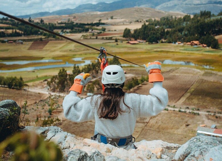 A person rappelling down a rocky cliff with a scenic view of a valley and mountains in the background. 2