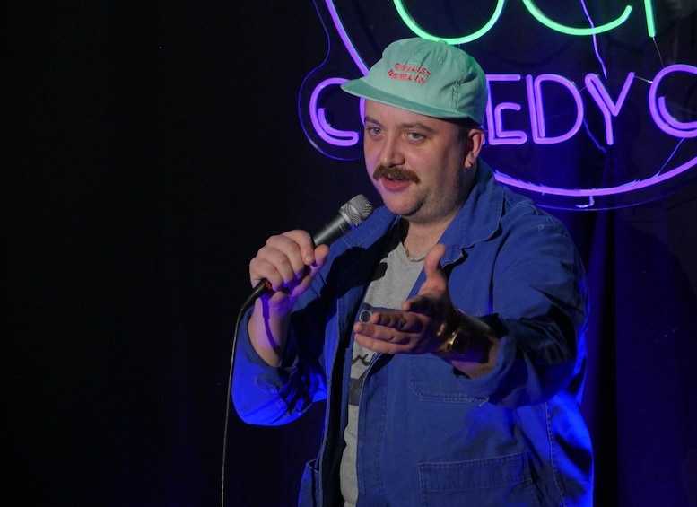 A person holding a microphone with a neon sign in the background. 5