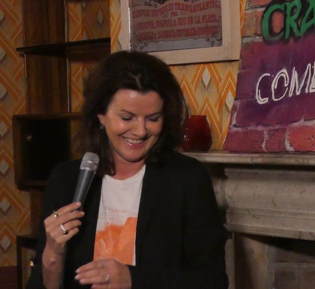 A person holding a microphone, standing in front of a wall with a graffiti-style sign. 3