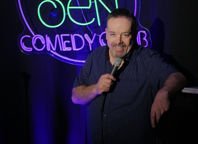 A person holding a microphone in front of a neon sign that reads 'COMEDY CLUB.' 4