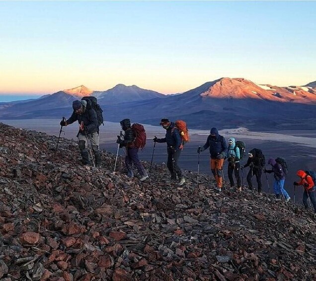 A group of hikers on a rocky mountain trail with a view of distant mountains. 3