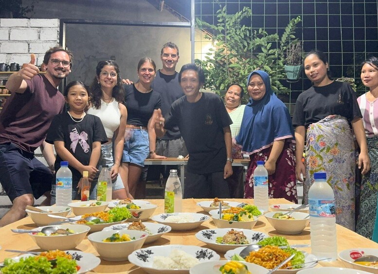 A group of people gathered around a table with various dishes, in an indoor setting with a brick wall and plants in the background. 2