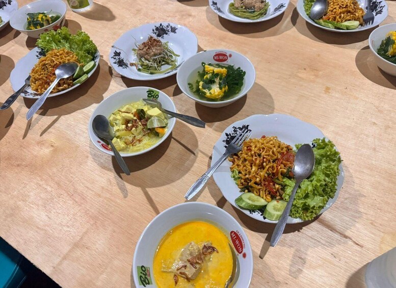 A table with various bowls of food, including noodles, vegetables, and soup. 3