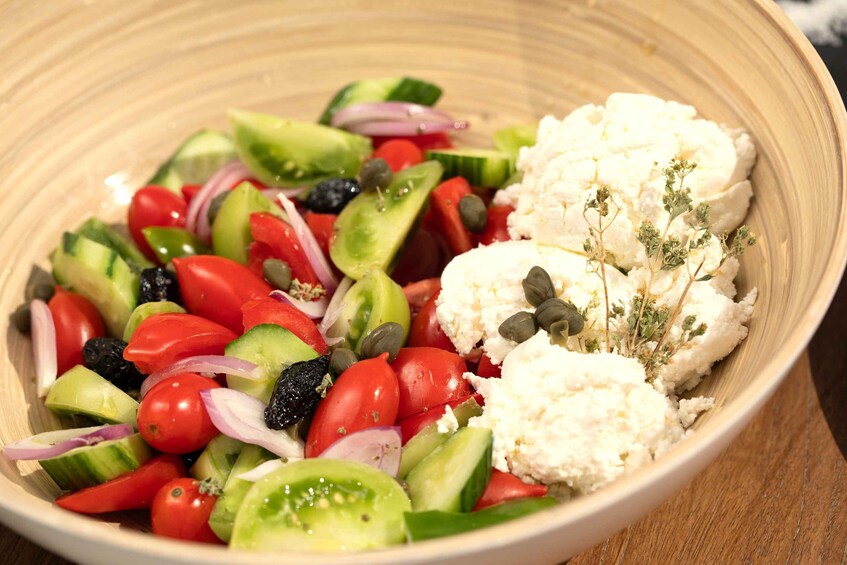 A bowl of salad with tomatoes, cucumbers, red onions, black olives, and cauliflower. 1