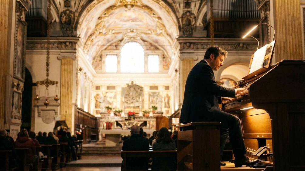Un uomo suona un pianoforte a coda in una chiesa con architettura ricca di decorazioni, mentre un pubblico è seduto. 2