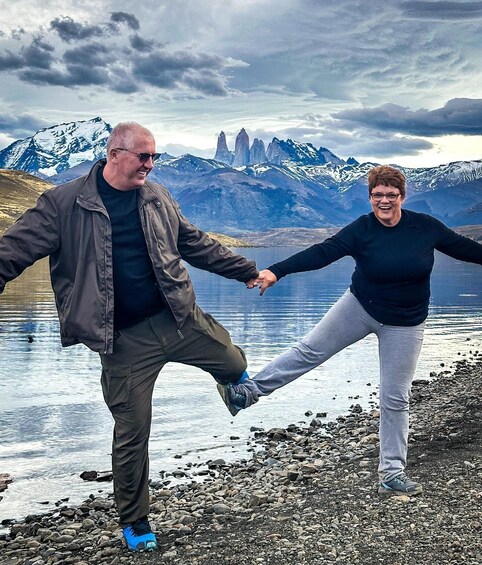 Two people holding hands on a rocky lakeshore with mountains in the background. 3