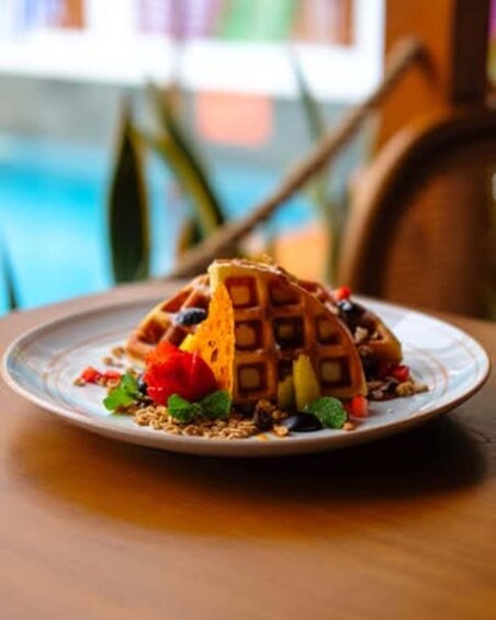 A plate with a waffle, strawberries, and mint leaves. 5