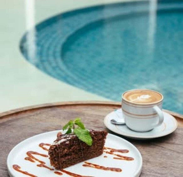 A slice of chocolate cake with a mint leaf on a white plate, accompanied by a cup of coffee with latte art on a wooden table. 3