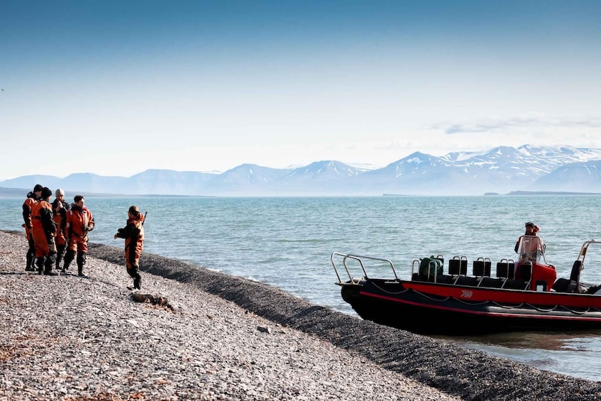 A group of people near a boat on a pebbly shore with mountains in the background. 5
