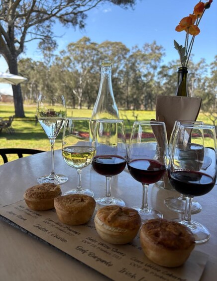 A table with wine glasses and pastries, outdoors with trees in the background. 1