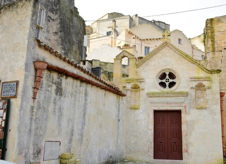 A weathered building with a red door and a small window, surrounded by older buildings. 4