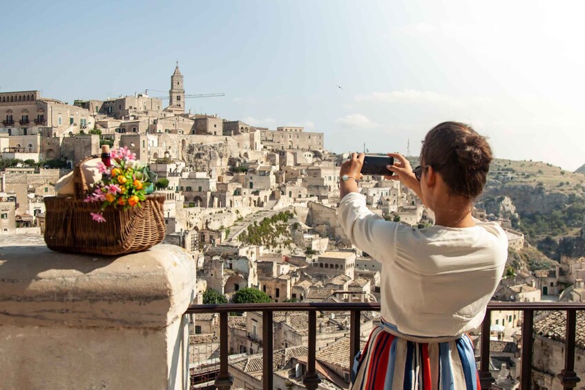 A person taking a photo of a historic cityscape with a wicker basket of flowers on a balcony. 1