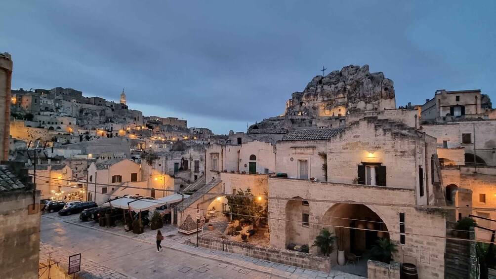 A historic town with stone buildings, a prominent rock formation, and a church with a cross on top. 5