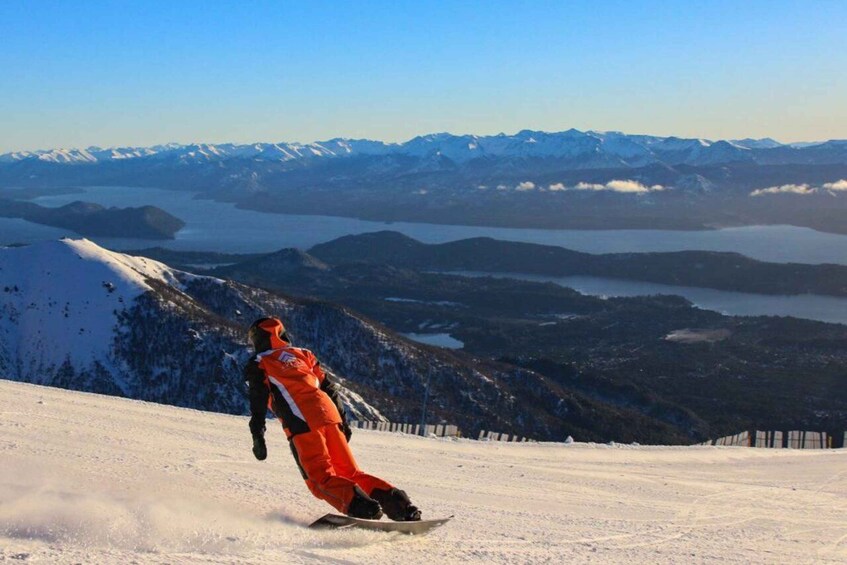 A snowboarder descending a snowy slope with a mountainous backdrop and a lake. 3