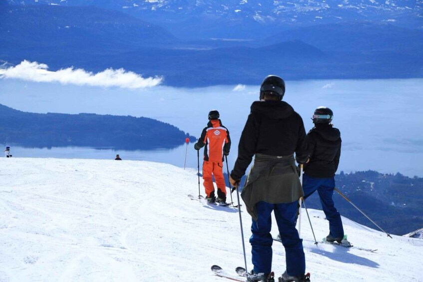 Skiers on a snowy slope with a lake and mountains in the background. 4