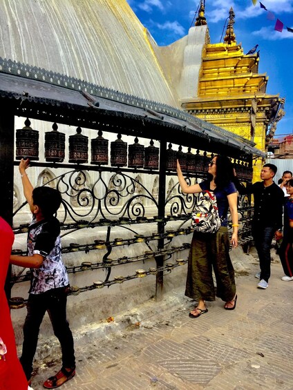 A group of people at a temple with prayer wheels and a golden structure in the background. 3