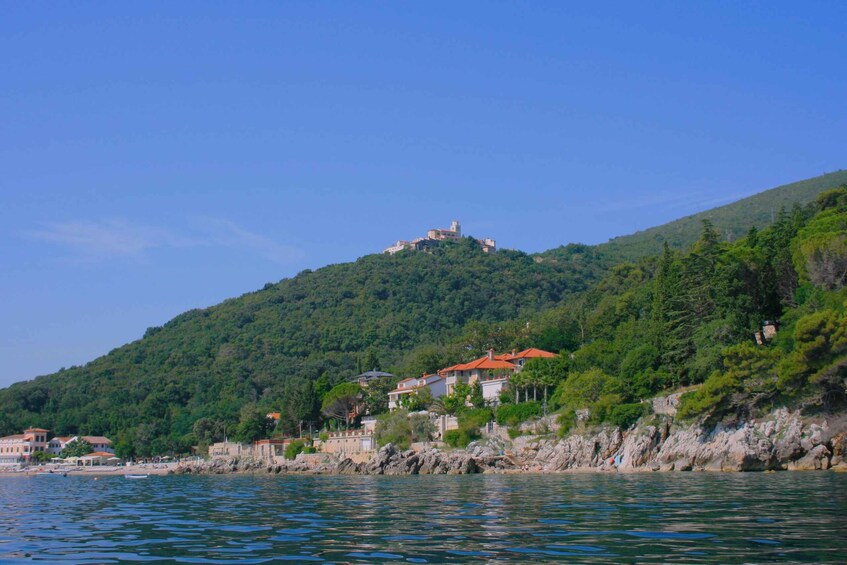 A coastal town with buildings on a hillside, a body of water in the foreground, and a hilltop structure. 3