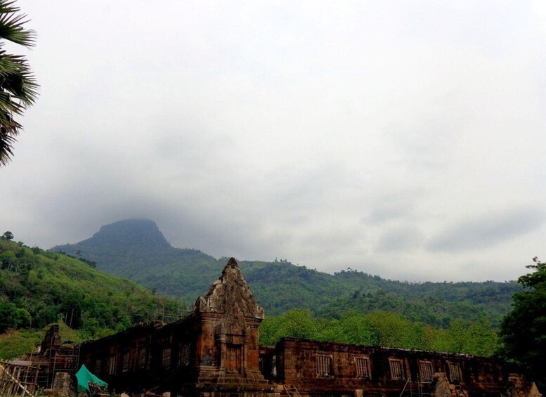 A historical stone structure with a pointed roof, surrounded by lush green hills and a cloudy sky. 2