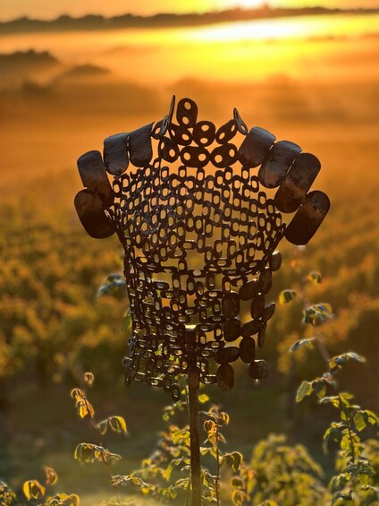 A metal sculpture with a complex geometric design, set against a backdrop of a sunset over a field. 2