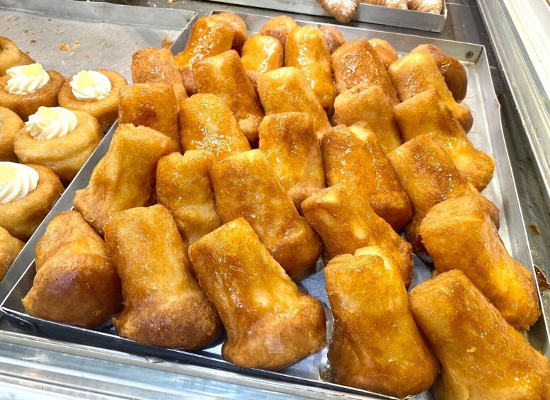 A display of golden-brown pastries, some with cream on top, in a metal tray. 4