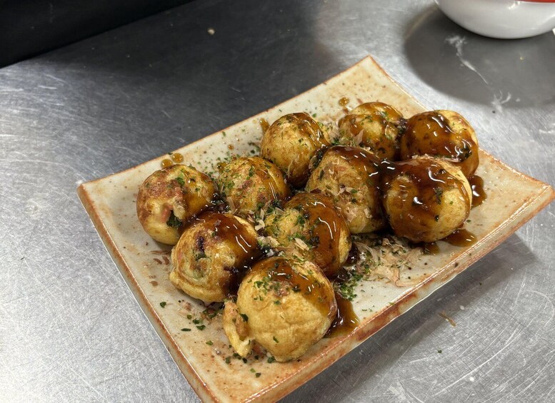 A plate of tempura balls with a dipping sauce, garnished with herbs, on a rectangular ceramic plate. 1