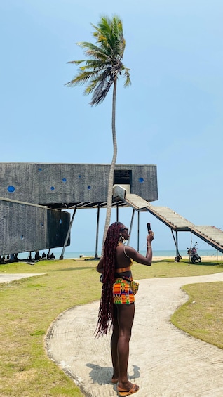 A person taking a photo with a smartphone, a palm tree, and a unique building structure. 1