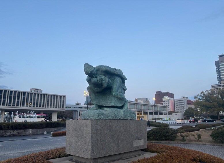 A bronze statue of a lion's head on a pedestal in an urban setting with modern buildings in the background. 4
