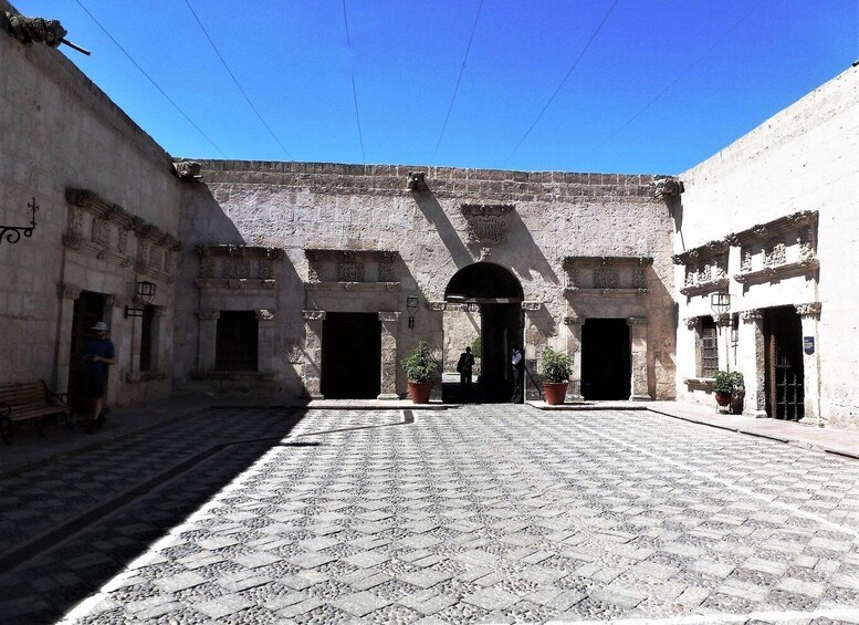 A courtyard with cobblestone pavement, a central archway, and buildings with stone facades. 5