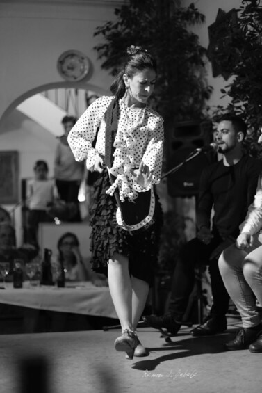 A person walking outdoors, dressed in a polka dot blouse and ruffled skirt, with a bow in their hair. 2