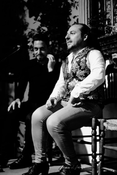 A person seated on a chair with a patterned vest and light-colored pants. 4