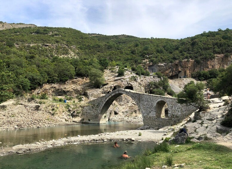 A stone bridge over a river, surrounded by greenery and rocky terrain. 2
