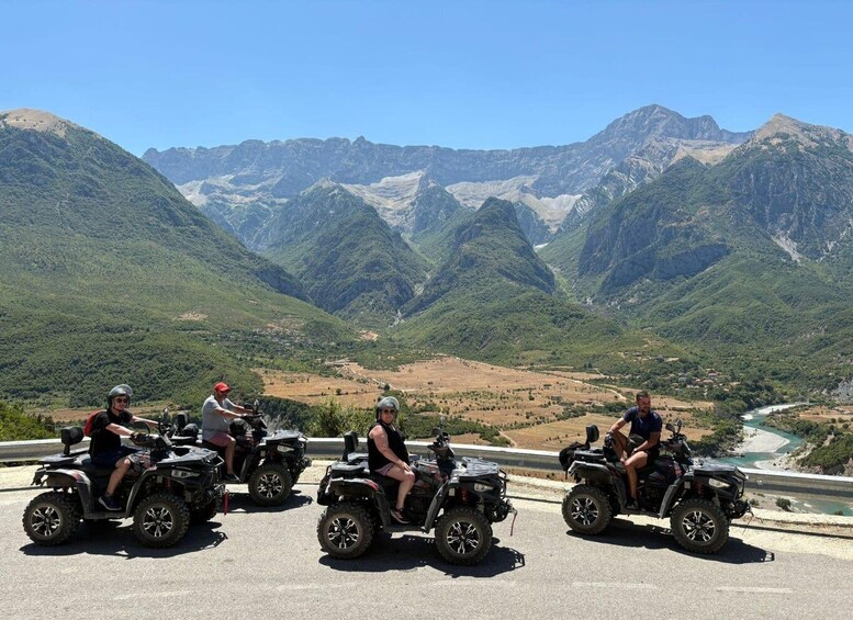 Four people on ATVs on a road with a mountainous landscape in the background. 5