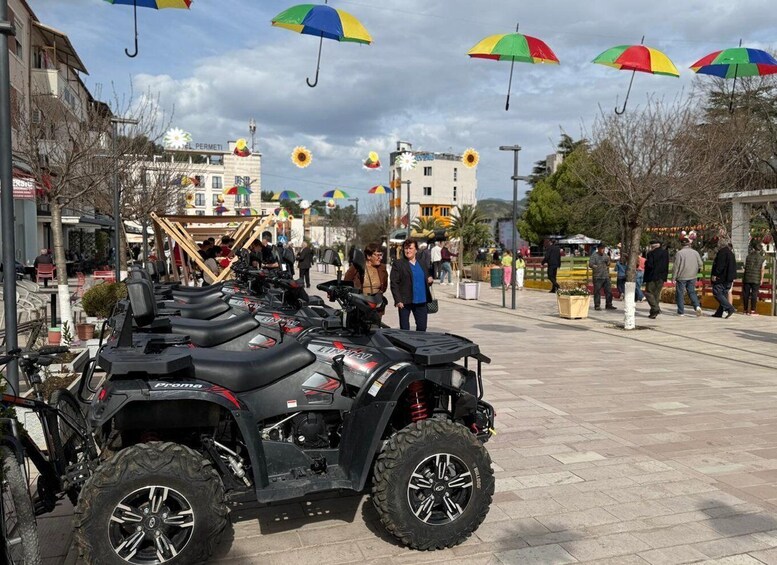 A paved square with ATVs parked in the foreground and colorful umbrellas hanging overhead. 1