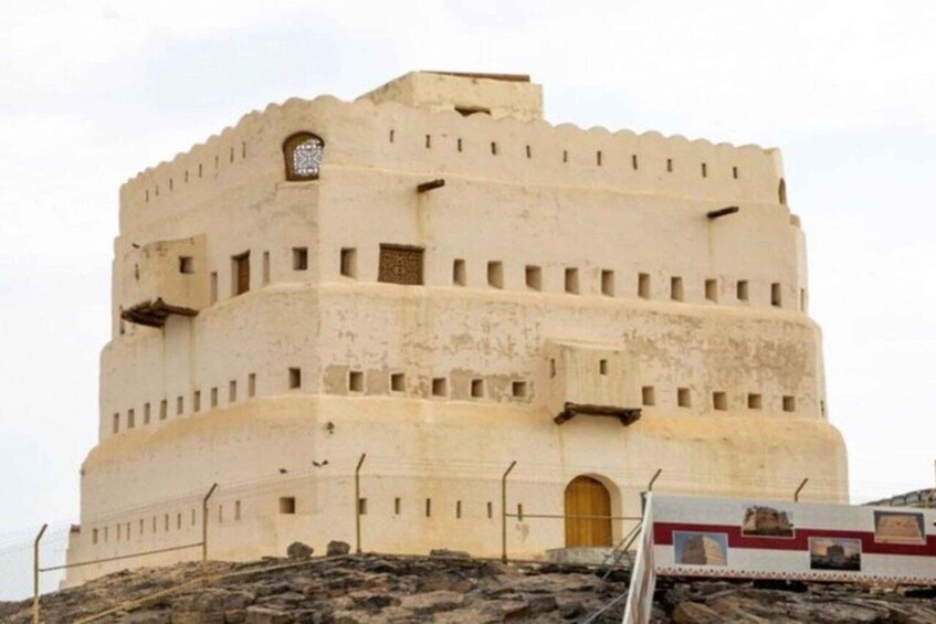 A large, beige, fortress-like building with a rounded tower and arched doorways. 4