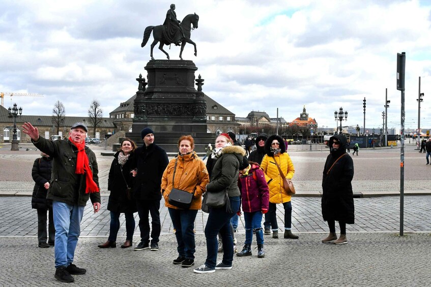A group of people standing in front of a statue of a man on horseback. 4