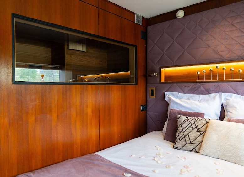 A bedroom with a wooden vanity, a bed with white linens, and a purple quilted headboard. 2