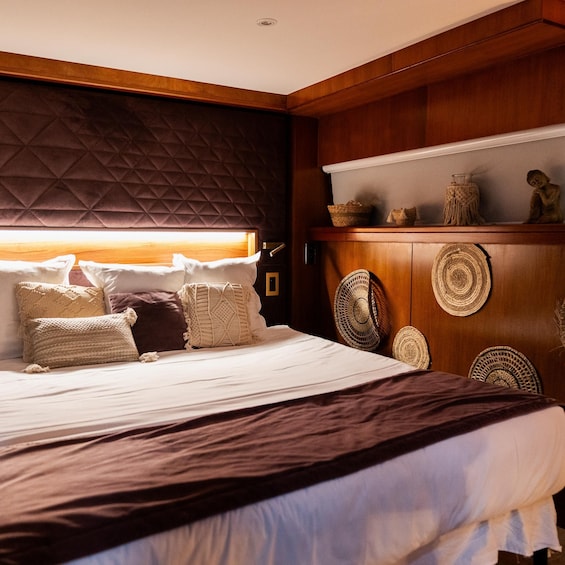 A bedroom with a bed, pillows, a headboard, a wooden cabinet with woven baskets, and a statue. 5