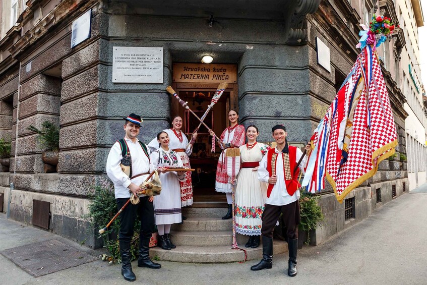 A group of people in traditional attire standing in front of a building with a sign that reads 'Hrvatska kuća MATERINA PRČA.' 4