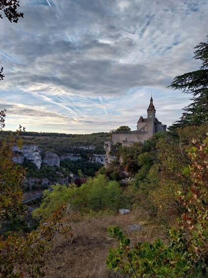 A historic stone building with a clock tower, surrounded by cliffs and autumn foliage. 4