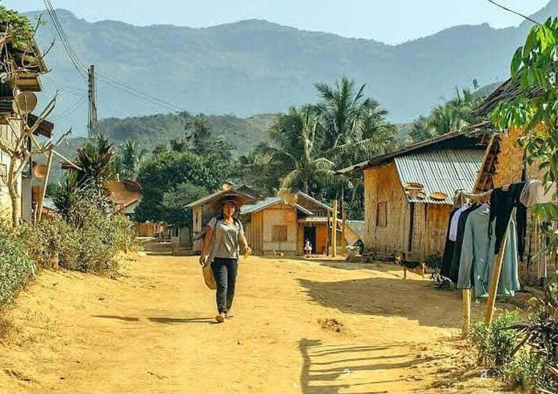 A person walking down a dirt road in a rural area with houses and mountains in the background. 1