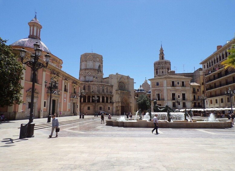 A historic plaza with a fountain, ornate buildings, and a clear blue sky. 2