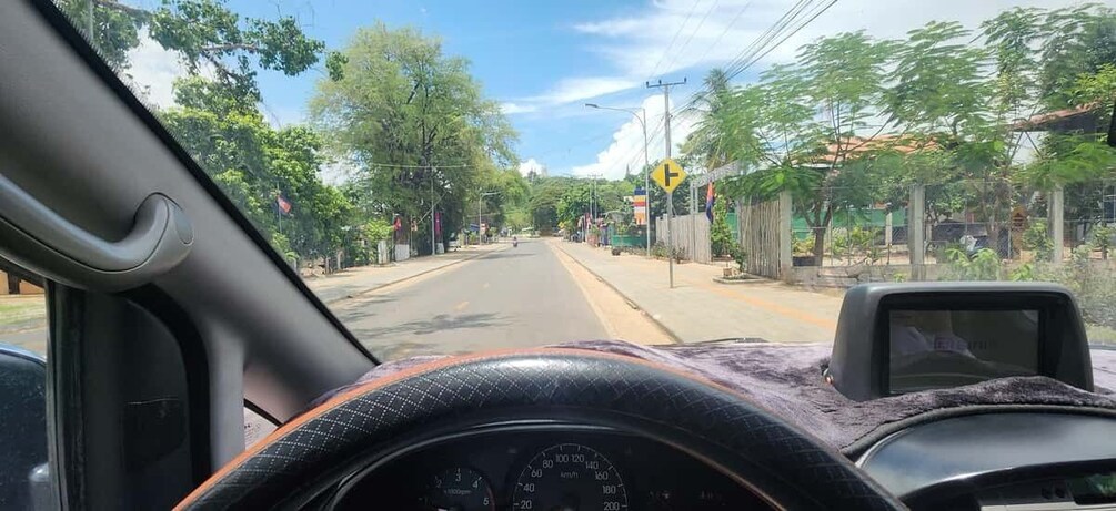 A car dashboard with a speedometer, a road with a yellow traffic sign, and trees lining the street. 3