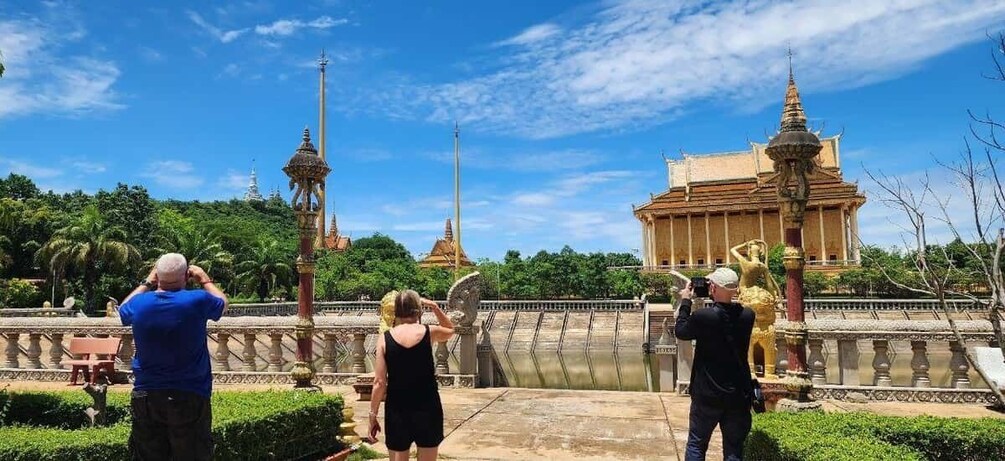 A group of people taking photographs of a temple with a tall spire and a golden statue in a garden. 5