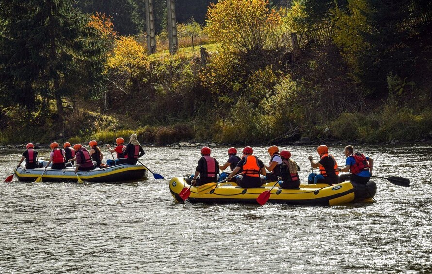Two groups of people in inflatable rafts on a river surrounded by trees. 3